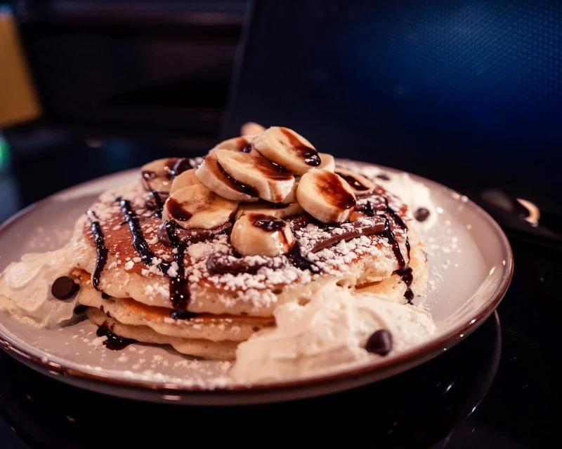 Banana and chocolate pancakes with whipped cream and powdered sugar